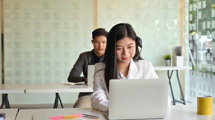Beautiful operator woman with headsets while working in a call center over colleague background.