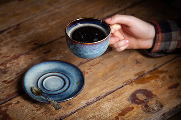Closeup black americano coffee in blue cup in male hand, saucer with vintage tea spoon on background wooden brown vintage village table. Concept morning breakfast lonely man, bachelor
