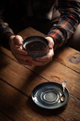 Fototapeta na wymiar Closeup black americano coffee in blue cup in male hand, saucer with vintage tea spoon on wooden brown vintage background. Concept breakfast in coffee house