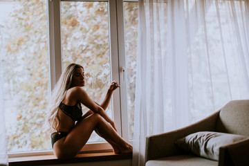Beautiful young woman in lingerie sitting and looking outside the window in beautiful apartment