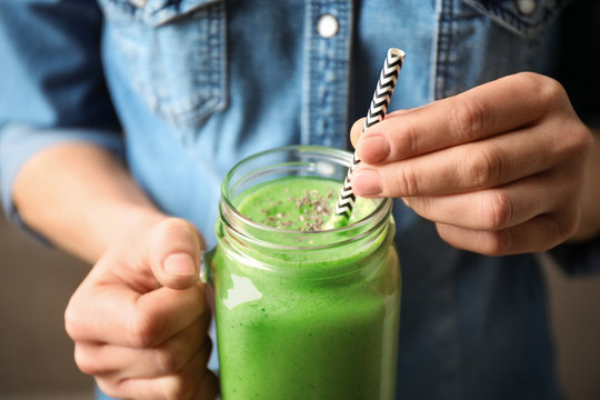 Woman holding tasty kale smoothie on brown background, closeup