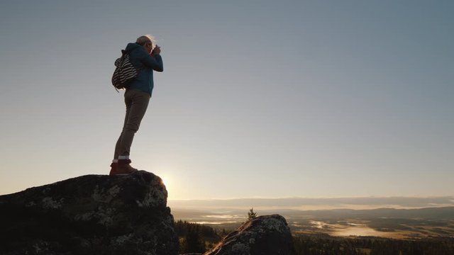 Woman on top of mountain takes pictures of beautiful landscape in Norway