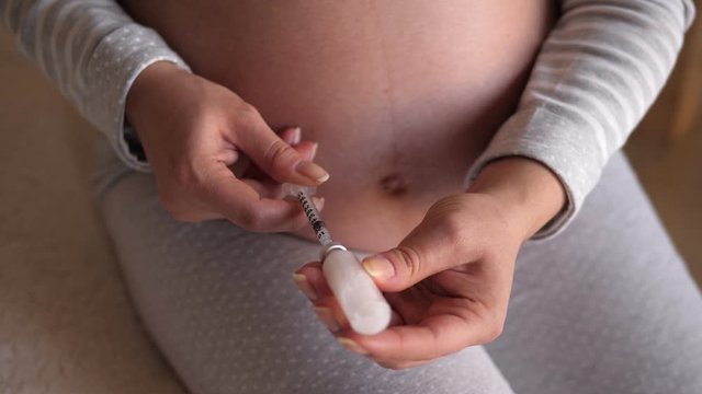 Close-up of a pregnant woman with diabetes gaining insulin in an insulin syringe. Pregnant woman makes injection of insulin in her belly. Diabetes and pregnancy health, sugar control.