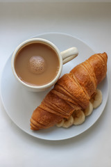coffee and croissant with banana on a white plate for breakfast