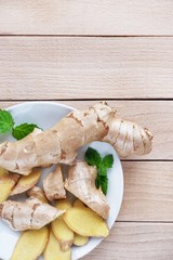 Fresh ginger root sliced and mint leaves on a white plate and a light wooden background. Vertical, Close-up, Top view with copy space for text.