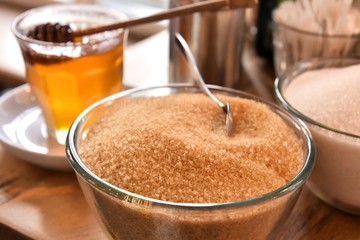 Additives to hot drinks.  Cane sugar, white sugar and honey with a special wooden spoon with selective focus on blurred background. Unhealthy carbohydrates. Brown and white sugar, organic honey