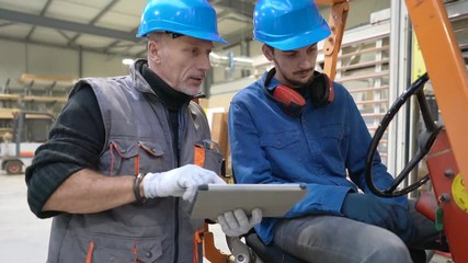 Man giving instructions to apprentice in warehouse, using cart