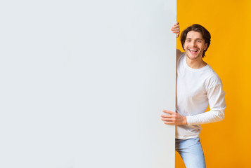 Positive young man holding big white advertisement board with copy space