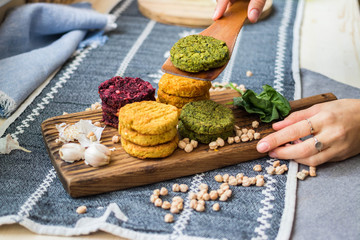 Vegan chickpea burgers cutlets or patties. Healthy vegan diet food. Woman hands holds mixed vegetables yellow pumpkin, orange carrot, green spinach and red beet bean cutlets with wooden spatula