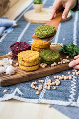 Obraz na płótnie Canvas Vegan chickpea burgers cutlets or patties. Healthy vegan diet food. Woman hands holds mixed vegetables yellow pumpkin, orange carrot, green spinach and red beet bean cutlets with wooden spatula