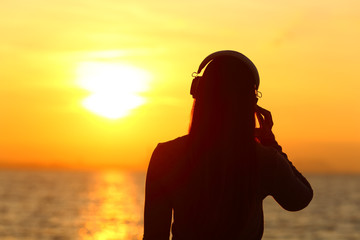 Girl wearing headphones listening to music at sunset
