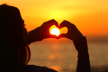 Girl hands silhouette making heart shape arround the sun