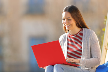 Happy student using red laptop sitting in a campus