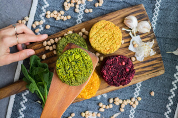 Vegan chickpea burgers cutlets or patties. Healthy vegan diet food. Woman hands holds mixed vegetables yellow pumpkin, orange carrot, green spinach and red beet bean cutlets with wooden spatula