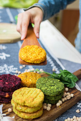Vegan chickpea burgers cutlets or patties. Healthy vegan diet food. Woman hands holds mixed vegetables yellow pumpkin, orange carrot, green spinach and red beet bean cutlets with wooden spatula