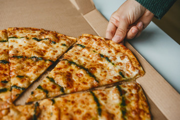 A person takes a piece of pizza from a box to eat