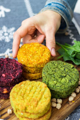 Vegan chickpea burgers cutlets or patties. Healthy vegan diet food. Woman holds in hand mixed vegetables yellow pumpkin, orange carrot, green spinach and red beet chickpea cutlets.