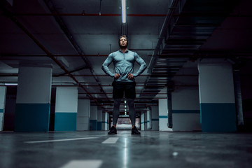 Low angle view of fit handsome caucasian sportsman in active wear standing in underground garage...
