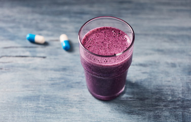 Glass of Protein Shake with milk and blueberries and Creatine capsules. Concept for Sport nutrition. Rustic wooden background. Close up. Copy space. 