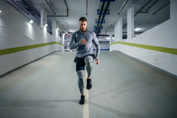 Young handsome powerful muscular caucasian sportsman in active wear running in underground garage at night. Urban life concept.