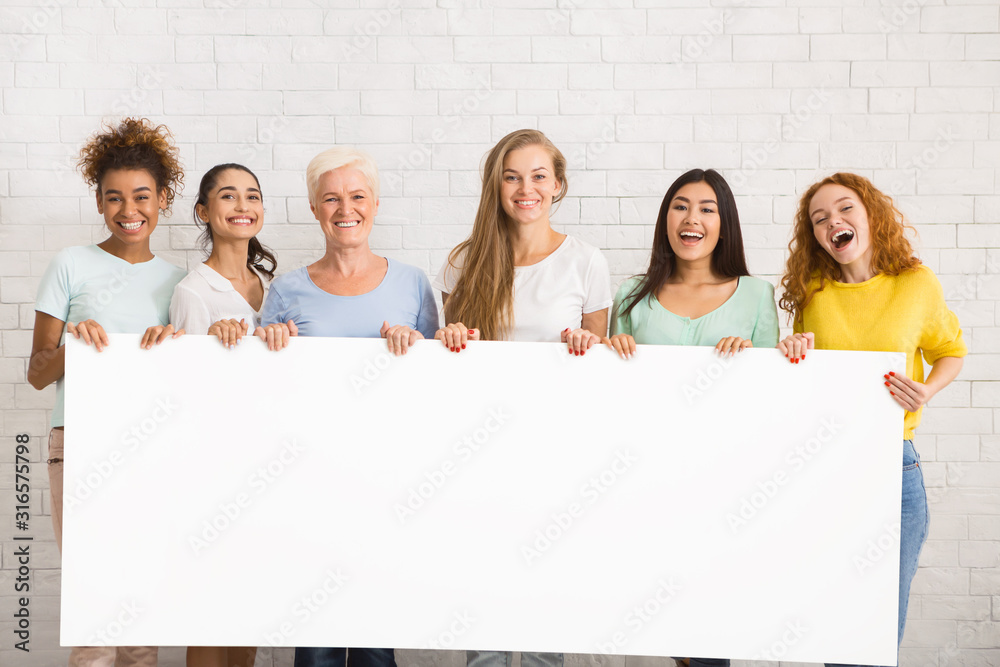 Wall mural women holding empty white poster standing over white wall, mockup