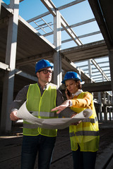 Two young architects on a construction site, discussing project details