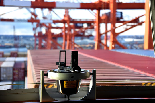 Gyro compass repeater on the cargo ship navigational bridge. Unfocused view of the containers and gantry cranes on the background. 