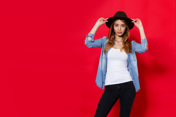 Beautiful girl in hat, posing with attitude in studio, isolaetd on a red background.