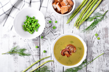 Vegetable pureed soup with asparagus and peas topped with roasted champignons on the white wooden table