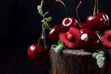 Ripe juicy cherries on tree stump against the black background