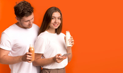Young couple drinking detox smoothies, girl using cellphone