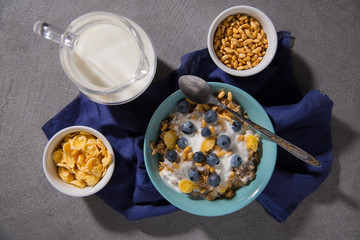 Bowl with granola and yogurt, cornflakes, blueberries and a glass of milk on a gray background