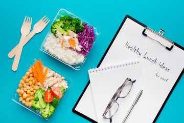 Lunch boxes with healthy food, notebook for notes, pen and glasses on a bright mint color paper background. The concept of healthy eating while working in the office.