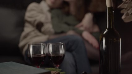 Bottle of wine and glasses and couple hugging on background, shallow depth of field