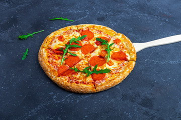 A fresh prepared pepperoni pizza with salami, tomatoes and cheese on a dark background. Italian traditional lunch or dinner. Fast food and street food concept. Flat ly, top view, copy space fot text