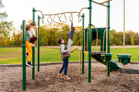 Mother assisting her daughter on the playgorund monkey bars - Powered by Adobe