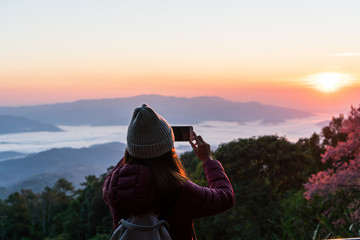 Fototapeta na wymiar Young Asian woman take a photo at beautiful sunrise and colorful sky in the mist over the mountain