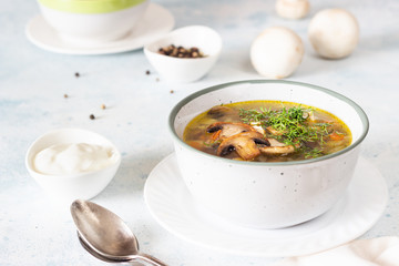 Homemade thick vegetarian mushroom soup with barley and vegetables with herbs in a ceramic bowl on a light grey stone background. Delicious cozy first course, comfort food.