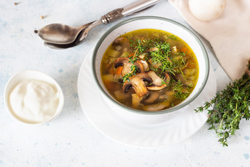 Homemade thick vegetarian mushroom soup with barley and vegetables with herbs in a ceramic bowl on a light grey stone background. Delicious cozy first course, comfort food.