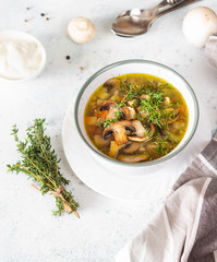 Homemade thick vegetarian mushroom soup with barley and vegetables with herbs in a ceramic bowl on a light grey stone background. Delicious cozy first course, comfort food.