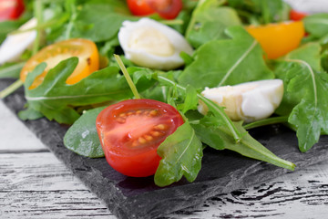 Salad with arugula, cherry tomatoes and quail eggs served on a slate plate