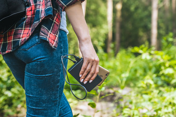 Power bank in a girl s hand, against the background of the forest and greenery.