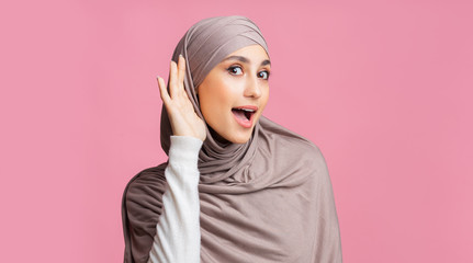 Interested muslim girl trying to hear information, holding hand near ear