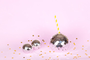 Creative disco cocktail shaped ball cup and paper straw, decorative bubbles and confetti with flash effect sparkle and shine on pink background. Concept for holidays and parties.