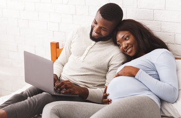 Lovely pregnant couple using laptop while resting