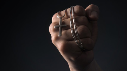 Close-up images of crucifix pendant and necklace in hand on black color background in studio which...