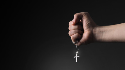 Close-up images of crucifix pendant and necklace in hand on black color background in studio which...