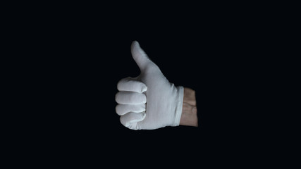 White-gloved hand on a black background. hand in white glove showing sign - thumb up, on black background, sign language