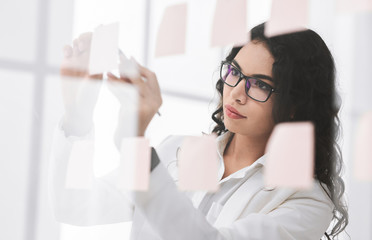 Hispanic manager writing on adhesive notes on glass wall