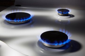 Burning blue gas on a white stove. Focus on the front edge of gas burners